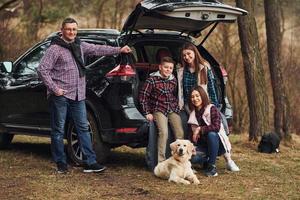 la familia feliz se divierte con su perro cerca de un camión moderno al aire libre en el bosque foto