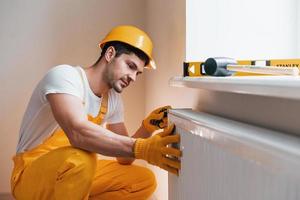 Handyman in yellow uniform installing new battery. House renovation conception photo