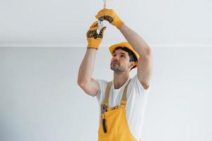 Handyman in yellow uniform changing light bulb. House renovation conception photo
