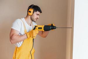 Handyman in yellow uniform works indoors by using hammer drill. House renovation conception photo