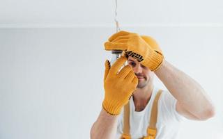 Handyman in yellow uniform changing light bulb. House renovation conception photo