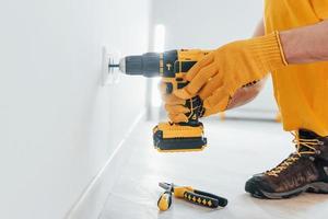 manitas en uniforme amarillo trabaja con electricidad e instala un nuevo enchufe usando un destornillador automático. concepción de renovación de la casa foto