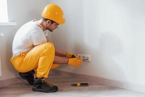 el manitas con uniforme amarillo trabaja con electricidad e instala un nuevo enchufe. concepción de renovación de la casa foto