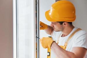 Handyman in yellow uniform installs new window. House renovation conception photo