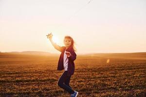 Happy little girl running with kite in hands on the beautiful field at sunrishe time photo