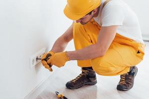 Handyman in yellow uniform works with electricity and installing new socket. House renovation conception photo