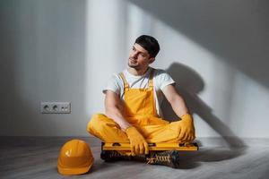 Tired handyman in yellow uniform sits indoors and takes break. House renovation conception photo