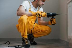 Handyman in yellow uniform works with drill indoors. House renovation conception photo