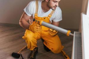 Handyman in yellow uniform works indoors with heat battery by using special tool. House renovation conception photo