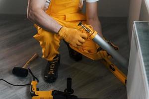 Handyman in yellow uniform works indoors with heat battery by using special tool. House renovation conception photo