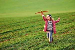 Cute little girl have fun with toy plane on the beautiful green field at sunny daytime photo