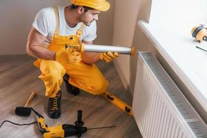 manitas en uniforme amarillo trabaja en interiores con batería de calor usando una herramienta especial. concepción de renovación de la casa foto