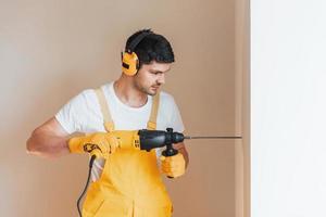 Handyman in yellow uniform works indoors by using hammer drill. House renovation conception photo