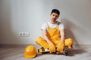 Tired handyman in yellow uniform sits indoors and takes break. House renovation conception photo