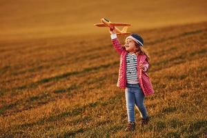 Illuminated by sunlight. Cute little girl have fun with toy plane on the beautiful field at daytime photo