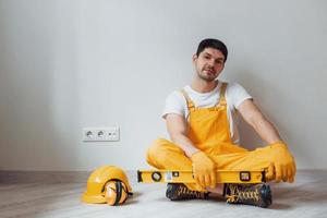 Tired handyman in yellow uniform sits indoors and takes break. House renovation conception photo