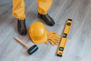 Tools on the floor. Handyman in yellow uniform standing indoors. House renovation conception photo