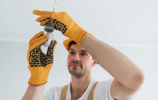 Handyman in yellow uniform changing light bulb. House renovation conception photo