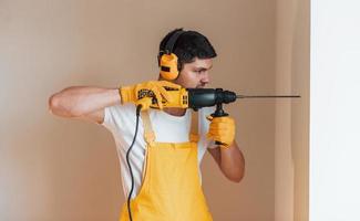 Handyman in yellow uniform works indoors by using hammer drill. House renovation conception photo