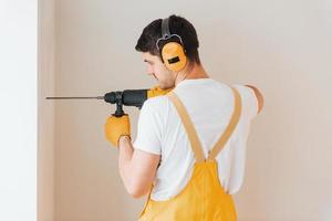 Handyman in yellow uniform works indoors by using hammer drill. House renovation conception photo