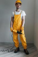 Handyman in yellow uniform with drill standing indoors. House renovation conception photo