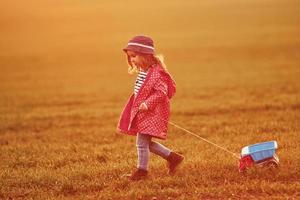 una linda niña camina con un camión de juguete en el hermoso campo durante el día soleado foto