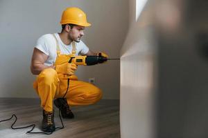 Handyman in yellow uniform works with drill indoors. House renovation conception photo