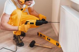 Handyman in yellow uniform works indoors by using hammer drill. House renovation conception photo