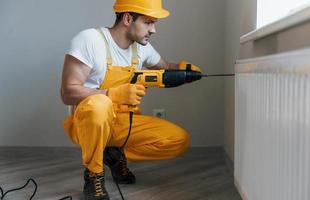 Handyman in yellow uniform works with drill indoors. House renovation conception photo