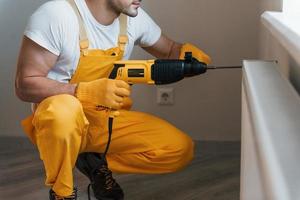 Handyman in yellow uniform works with drill indoors. House renovation conception photo