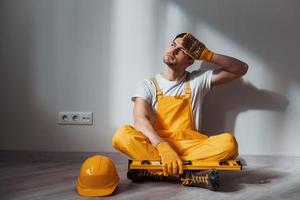 el manitas cansado con uniforme amarillo se sienta en el interior y toma un descanso. concepción de renovación de la casa foto