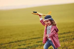 Cute little girl have fun with toy plane on the beautiful green field at sunny daytime photo