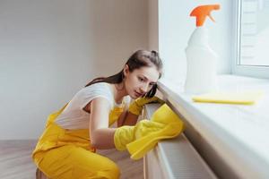 ama de casa en uniforme amarillo trabaja con limpiador de ventanas y superficies en interiores. concepción de renovación de la casa foto