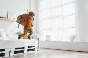 Little boy in retro pilot uniform running with toy plane indoors photo