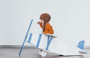 Little boy in retro pilot uniform having fun with toy plane indoors photo