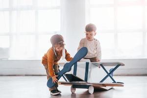 Two little boys in retro pilot uniform having fun with toy plane indoors photo