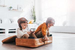 Two little boys have fun and sitting in suitcase indoors at daytime photo
