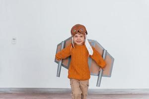 Little boy in retro pilot uniform running with toy plane indoors photo