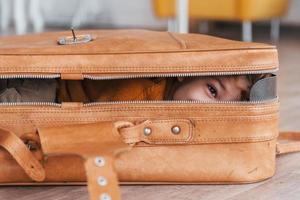 los niños pequeños con traje de piloto retro se divierten y se acuestan en una maleta en el interior durante el día foto