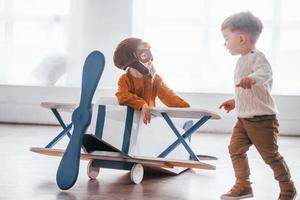 Two little boys in retro pilot uniform having fun with toy plane indoors photo