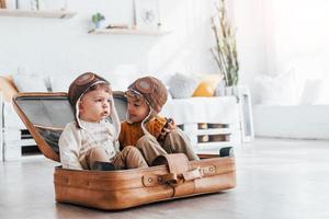 Two little boys have fun and sitting in suitcase indoors at daytime photo