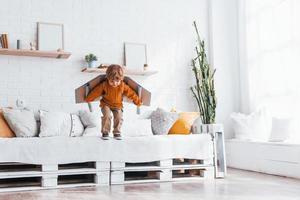 Little boy in retro pilot uniform running with toy plane indoors photo