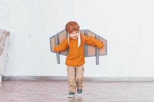 Little boy in retro pilot uniform running with toy plane indoors photo