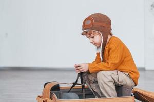 Little boys in retro pilot costume have fun and sitting in suitcase indoors at daytime photo