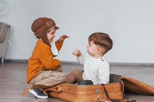 Two little boys have fun and sitting in suitcase indoors at daytime photo