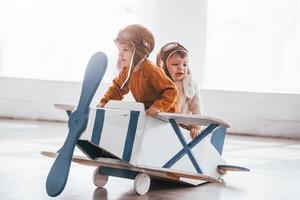 Two little boys in retro pilot uniform having fun with toy plane indoors photo