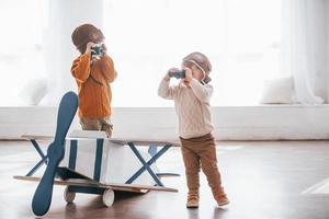 Two little boys in retro pilot uniform having fun with toy plane indoors photo