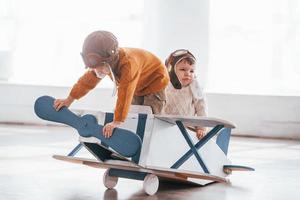 Two little boys in retro pilot uniform having fun with toy plane indoors photo