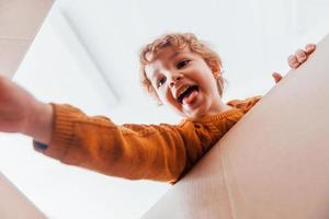 vista desde abajo de un niño con el pelo rizado que se divierte con una caja de papel en el interior foto