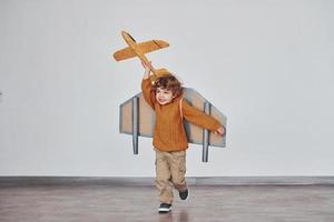 Little boy in retro pilot uniform running with toy plane indoors photo